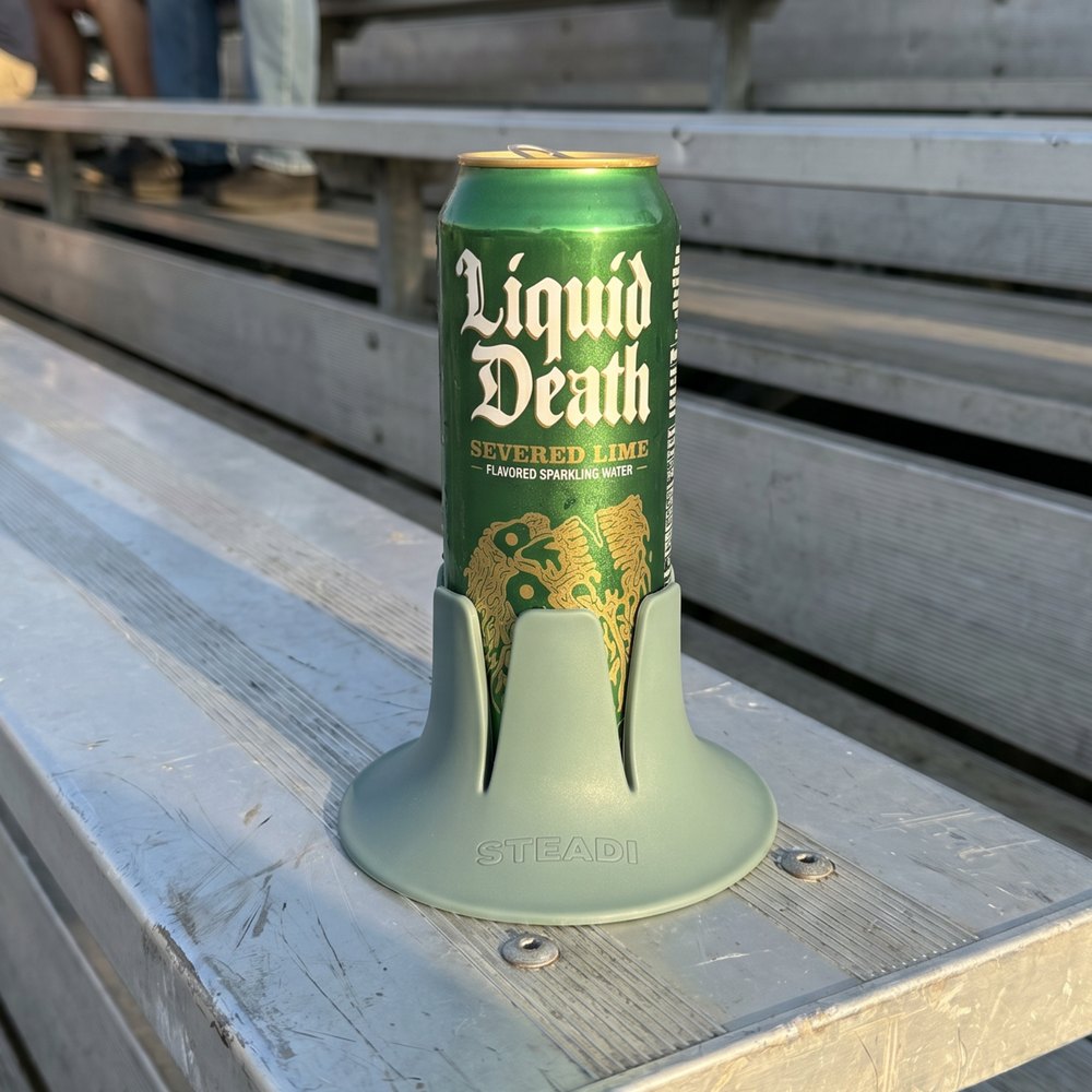 A can standing in a sage Steadi on a plank bench at a venue, people seated behind.
